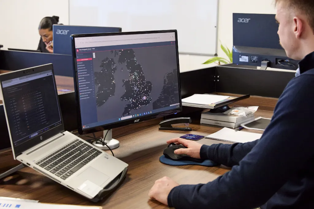 Man using a computer workstation to monitor a UK map dashboard on dual screens