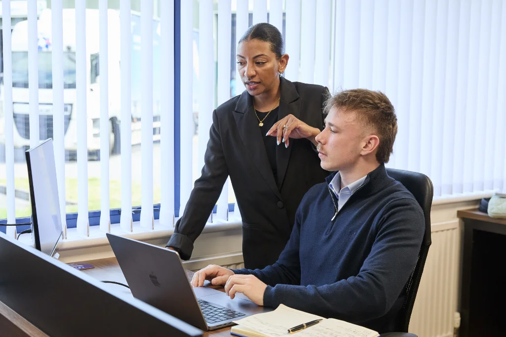 Colleagues working together at desk using laptop in office environment