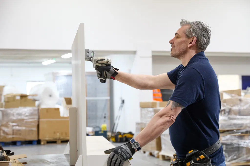 Man assembling a retail display unit with a drill in a workshop
