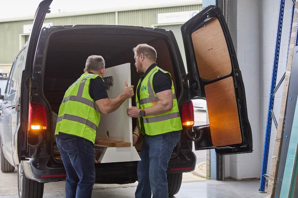 Two SJH staff wearing hi-vis loading large item into back of a van