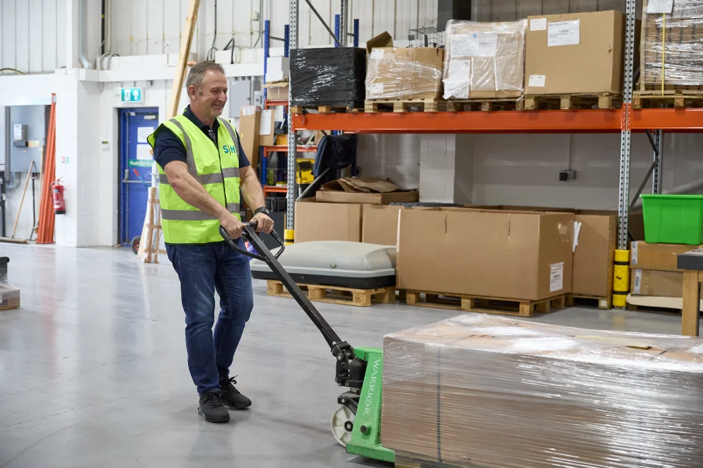Warehouse worker using manual pallet truck to move wrapped goods
